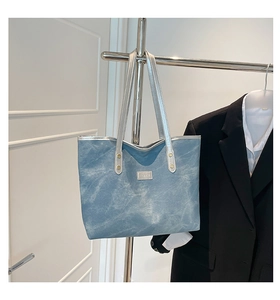 Dettaglio della borsa tote in denim azzurro con manici argento lucido ed etichetta moda