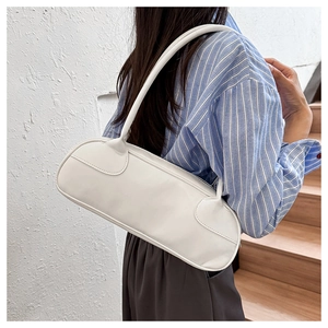 Detail view of a minimalist cream white baguette bag worn on a woman's shoulder