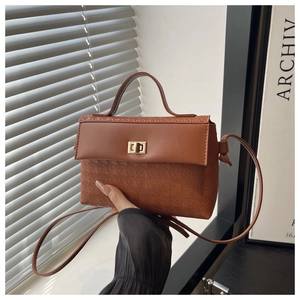 Close-up of brown textured crossbody bag with gold twist lock and embossed geometric pattern
