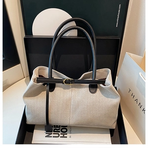 Detail of cream woven tote bag featuring black leather straps and gold metal buckle