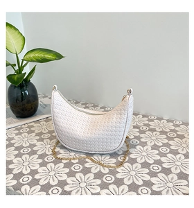 Detail of white woven crescent bag with gold chain strap on a vintage table
