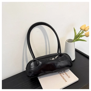 Minimalist black baguette bag with glossy leather finish shown in a modern home setting