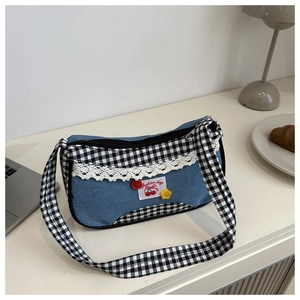 Detail of blue denim shoulder bag with white lace trim and cherry patch on a white desk