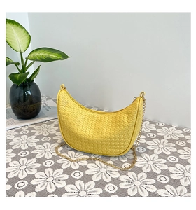 Macro detail of yellow woven leather dumpling bag with elegant gold chain strap
