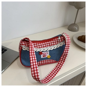 Detail of red gingham and denim shoulder bag with lace trim and cherry patch on a desk