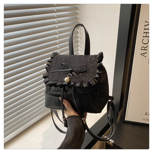 Detail of black mini backpack featuring lace ruffles, silk bow, and faux pearl pendant