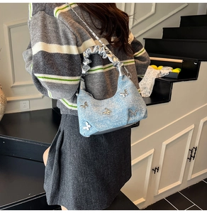 Detail of light blue denim hobo bag with silver butterfly patches and cloud handle