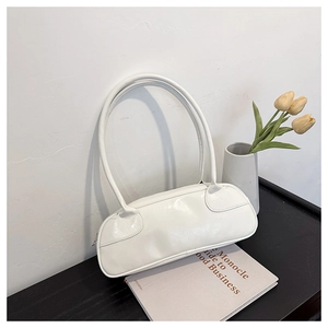 Detail of white glossy leather baguette bag with dual long shoulder straps on books
