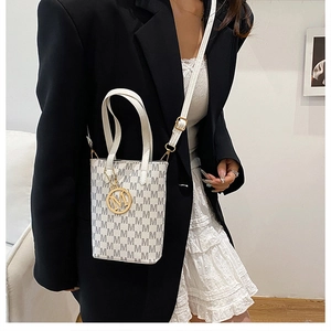 Detail of white mini tote bag with gold M-logo pendant worn on a black blazer