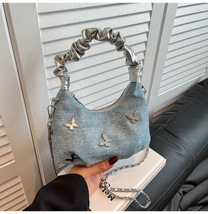 Detail of light blue denim underarm bag with silver butterfly charms and ruched handle