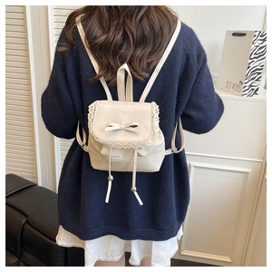 Detail of cream mini backpack with lace trim, bow flap, and beaded drawstring accents