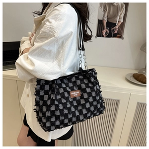 Detail of checkered denim tote bag with frayed edges and fashion leather patch detail