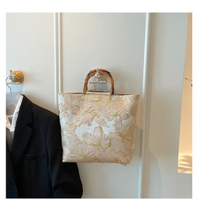 Detail of floral jacquard tote bag with natural bamboo handles and gold-pink texture