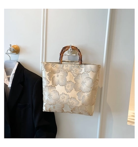 Detail of floral embroidery on beige tote bag with natural bamboo handle texture