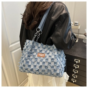 Détail d'un sac cabas en denim à damier bleu avec bords effilochés et étiquette en cuir brun