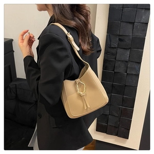Detail of beige PU shoulder bag with wavy gold buckle and leather tassels on a model