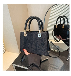 Detail of black jacquard handbag with embossed floral texture and gold-tone metal hardware