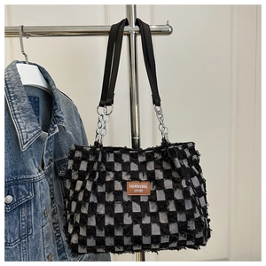 Detail of plaid denim tote bag featuring fringe edges and metal chain leather strap