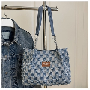 Detail of blue checkerboard denim tote bag with leather tag and metal chain strap