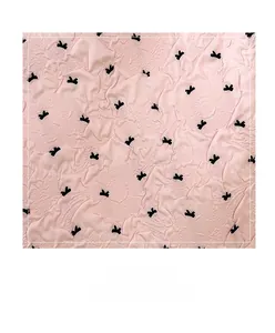 Détail du tissu rose à texture gaufrée avec des motifs de petits nœuds noirs et fini doux