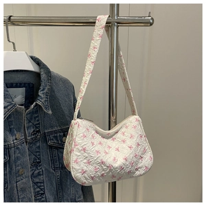 Detail of white crossbody bag featuring pink bow patterns and embossed wrinkled texture