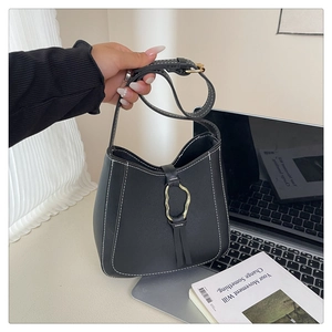 Detail of black bucket bag with white stitching, gold ring buckle, and leather tassel charm