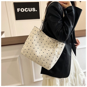 On-shoulder view of white bow-embroidered tote bag with pearl pendant and chain strap