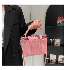 Détail d'un sac à main tressé rose avec logo métallique doré en V et texture PU