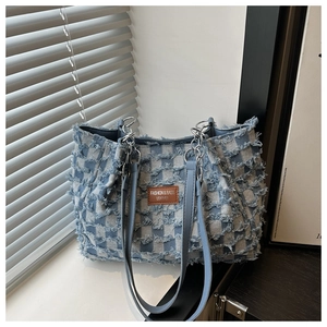 Detail der karierten Denim-Tragetasche mit Fransentextur, Lederetikett und Kettenriemen