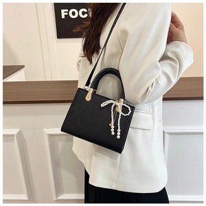 Black litchi grain shoulder bag featuring a delicate pearl bow charm on the side