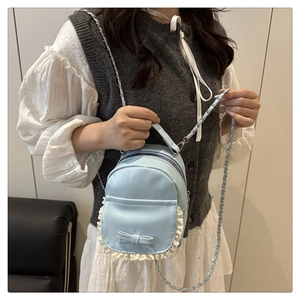 Close-up of light blue mini backpack with lace trim and bow accent on a model