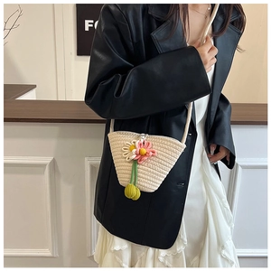 Detail der beige Stroh-Eimertasche mit 3D-Blumenanhängern und Quasten-Akzenten