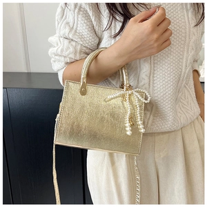 Metallic gold square bag with pearl bow charm worn over a cream knit sweater
