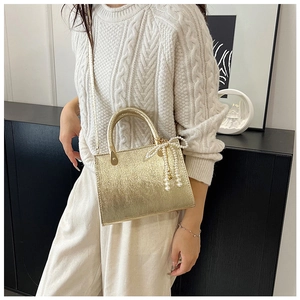 Detail of metallic gold crossbody bag with elegant pearl bow charm and top handle