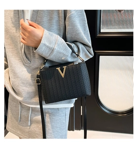 Détail du sac à bandoulière tissé noir avec boucle en V dorée et bandoulière fine