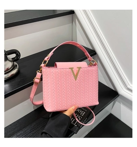 Détail du sac à main rose tressé avec logo V doré et bandoulière sur un escalier