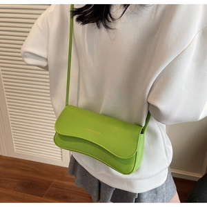 Detail of bright green leather baguette bag worn over the shoulder against a white door