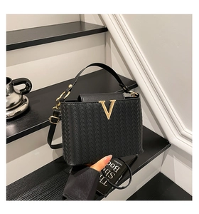 Détail de la texture tressée noire et boucle en métal doré en V sur le sac à main