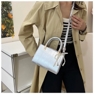 Close-up of silver crossbody bag with metal handles and a pearl bow charm on a model