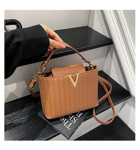 Détail d'un sac à main marron à texture tressée avec boucle métallique dorée en V chic