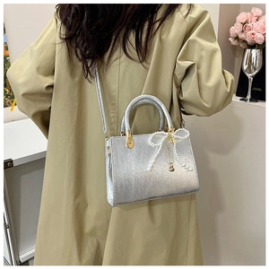 Silver glitter crossbody bag with pearl bow charm worn over a khaki jacket