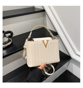 Détail du sac à main tissé crème avec logo V doré sur des escaliers avec un café