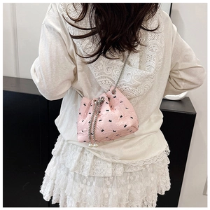 Detail of pink bow bucket bag with pearl drawstring and metal chain strap shown on shoulder