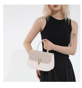 Detalle de bolso elegante color crema con solapa trenzada y cierre de herradura dorado fino