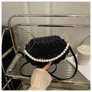 Detail of shell-shaped black crossbody bag with snakeskin texture and pearl handle