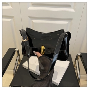 Detail of black patent leather underarm bag with gold buckle on white books background