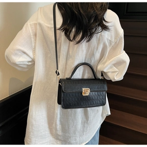 Detail of black crocodile texture handbag with gold buckle held by model in white shirt