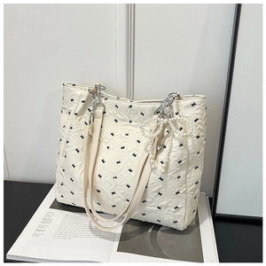 Detail of cream tote bag with black bow embroidery, silver chain strap, and pearl charm