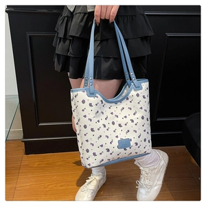 Detail of white floral tote bag with blue trim and metal rivets shown on a model