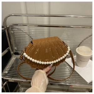 Macro detail of brown shell-shaped crossbody bag with pearl handle and snake texture